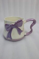 Four pastel ceramic coffee mugs with cute 3D bows and heart-shaped handles lined up on a kitchen counter.