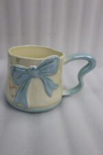 Four pastel ceramic coffee mugs with cute 3D bows and heart-shaped handles lined up on a kitchen counter.