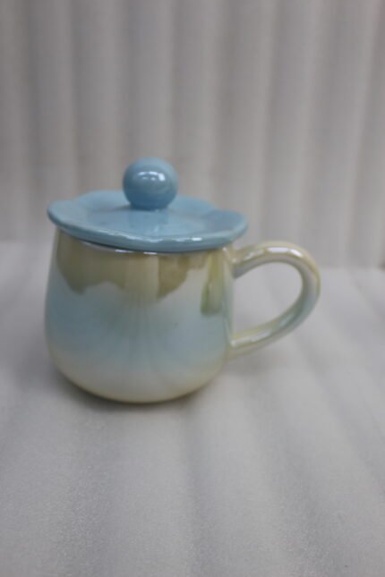 Four colorful pastel ceramic mugs with matching lids featuring sphere knobs, arranged neatly on a marble kitchen countertop with cinematic lighting