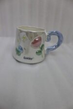 Two glazed ceramic mugs with embossed 3D flowers, stars, and pastel pink and blue artistic handles placed on a kitchen counter.
