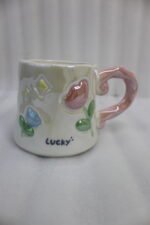 Two glazed ceramic mugs with embossed 3D flowers, stars, and pastel pink and blue artistic handles placed on a kitchen counter.