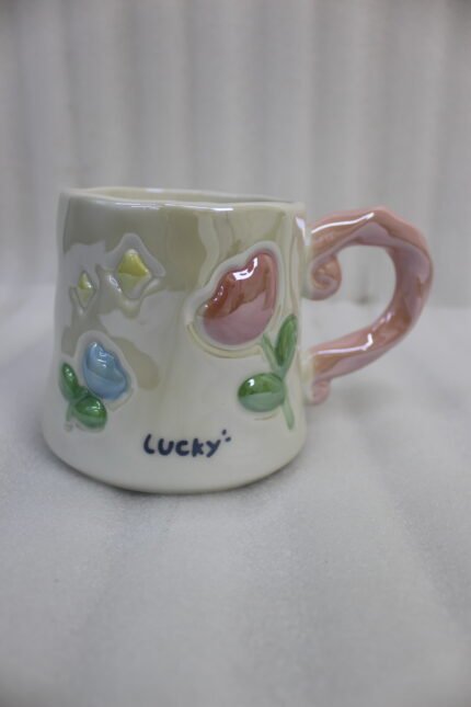 Two glazed ceramic mugs with embossed 3D flowers, stars, and pastel pink and blue artistic handles placed on a kitchen counter.