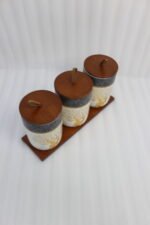 Three white and speckled black kitchen storage canisters featuring a gold deer and tree motif, fitted with wooden lids with loop handles and arranged on a matching wooden tray on a kitchen counter.
