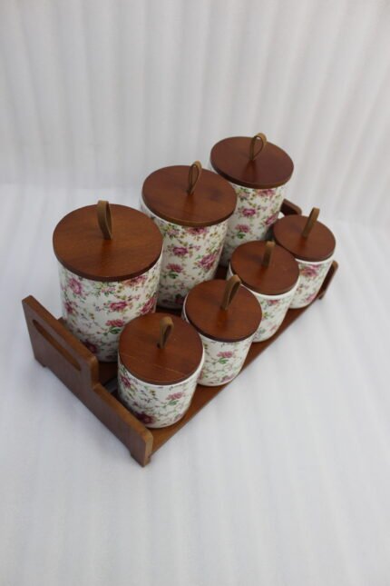 Floral ceramic kitchen canister and jar set with wooden lids and display stand on a kitchen counter
