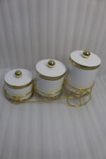 A set of three white ceramic jars with gold lids and spherical handles, elegantly arranged in a decorative gold metal cart stand against a white background.