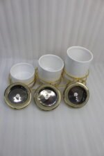 A set of three white ceramic jars with gold lids and spherical handles, elegantly arranged in a decorative gold metal cart stand against a white background.