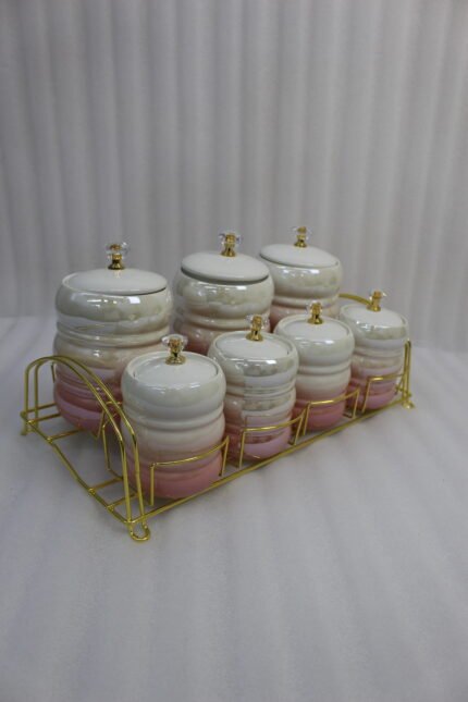 Luxury pink and white ceramic storage jar set with crystal knobs arranged on a modern gold wire rack on a kitchen countertop.