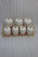 Luxury pink and white ceramic storage jar set with crystal knobs arranged on a modern gold wire rack on a kitchen countertop.