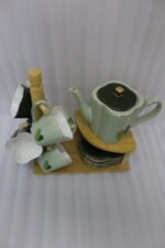 Green and black ceramic tea set with 6 cups, kettle, saucers, and a wooden display stand on a kitchen counter