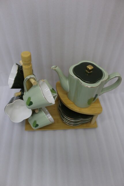 Green and black ceramic tea set with 6 cups, kettle, saucers, and a wooden display stand on a kitchen counter