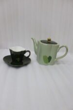Green and black ceramic tea set with 6 cups, kettle, saucers, and a wooden display stand on a kitchen counter