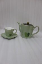 Green and black ceramic tea set with 6 cups, kettle, saucers, and a wooden display stand on a kitchen counter