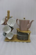 Pink and pastel ceramic tea set featuring 6 cups, 1 kettle, and a stacked saucer tier organized on a wooden display stand and tray on a kitchen counter.