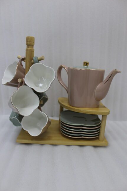 Pink and pastel ceramic tea set featuring 6 cups, 1 kettle, and a stacked saucer tier organized on a wooden display stand and tray on a kitchen counter.