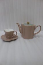 Pink and pastel ceramic tea set featuring 6 cups, 1 kettle, and a stacked saucer tier organized on a wooden display stand and tray on a kitchen counter.