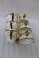 White ceramic tea cups and saucers neatly organized on a luxury golden stand on a marble kitchen countertop.