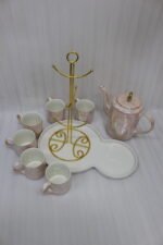 Luxury iridescent ceramic tea set with 6 cups, kettle, white ceramic tray, and golden display stand on a kitchen counter.