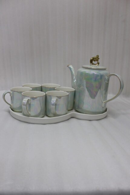 Luxurious iridescent ceramic tea set featuring six cups, one kettle, and a gold-finish stand on a white tray, arranged on a marble kitchen counter.