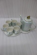 Luxurious iridescent ceramic tea set featuring six cups, one kettle, and a gold-finish stand on a white tray, arranged on a marble kitchen counter.