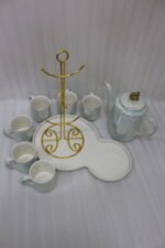 Luxurious iridescent ceramic tea set featuring six cups, one kettle, and a gold-finish stand on a white tray, arranged on a marble kitchen counter.