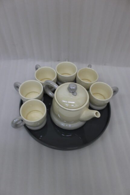 Ceramic rotating tray tea set with six cups and a kettle arranged neatly on a modern kitchen countertop.