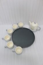 Ceramic rotating tray tea set with six cups and a kettle arranged neatly on a modern kitchen countertop.