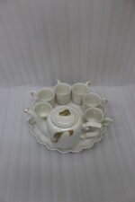White and gold ceramic tea set with 6 cups, 1 kettle, and a rotating tray displayed on a kitchen counter.