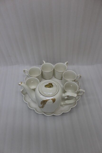 White and gold ceramic tea set with 6 cups, 1 kettle, and a rotating tray displayed on a kitchen counter.