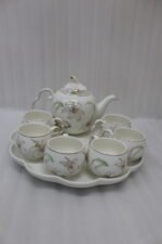 Elegant floral ceramic tea set featuring one kettle, six matching cups, and a smooth rotating tray on a kitchen counter.