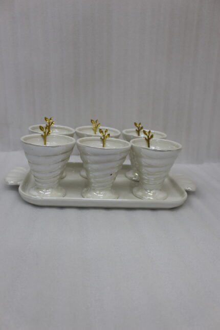 White ceramic ice cream set with 6 swirled pedestal bowls, matching serving tray, and gold leaf spoons displayed on a marble kitchen counter.