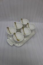 White ceramic ice cream set with 6 swirled pedestal bowls, matching serving tray, and gold leaf spoons displayed on a marble kitchen counter.