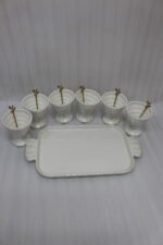 White ceramic ice cream set with 6 swirled pedestal bowls, matching serving tray, and gold leaf spoons displayed on a marble kitchen counter.