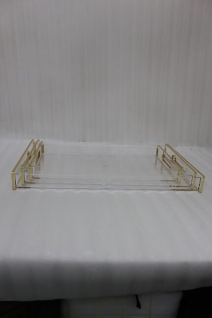 Nesting clear acrylic serving tray set with polished gold handles displayed on a white marble kitchen countertop.