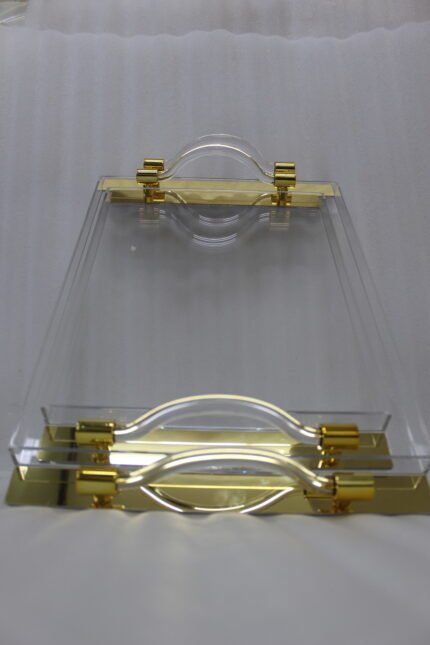 Luxurious clear acrylic serving tray set with polished gold handles and curved design, displayed on a marble countertop in a modern kitchen