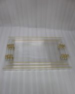 A nested set of clear ribbed acrylic serving trays with elegant gold handles and accents, displayed on a modern marble kitchen countertop next to glass spice jars.