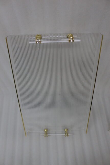 A nested set of clear ribbed acrylic serving trays with elegant gold handles and accents, displayed on a modern marble kitchen countertop next to glass spice jars.
