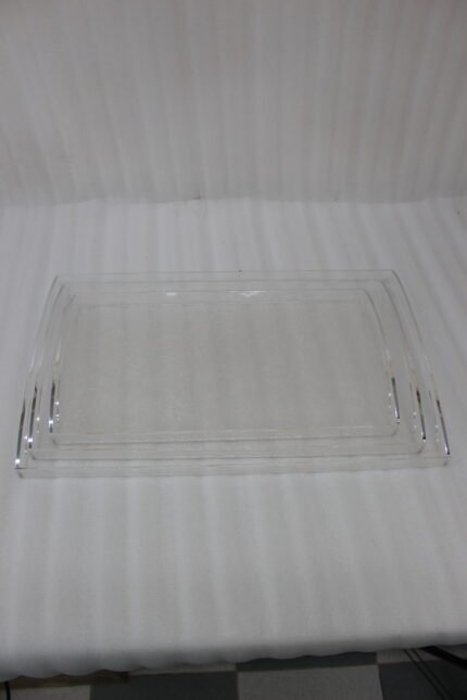 Set of clear acrylic serving trays with built-in handles and textured bases displayed on a marble kitchen counter next to an espresso machine and ceramic cups.