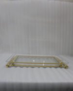 Two stacked luxury clear acrylic serving trays with polished gold trim and feet displayed on a white marble kitchen island.