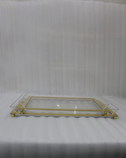 Two stacked luxury clear acrylic serving trays with polished gold trim and feet displayed on a white marble kitchen island.