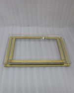 Two stacked luxury clear acrylic serving trays with polished gold trim and feet displayed on a white marble kitchen island.