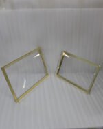 Two stacked luxury clear acrylic serving trays with polished gold trim and feet displayed on a white marble kitchen island.