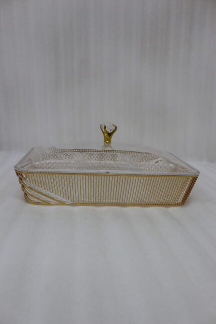 Elegant partitioned glass dry fruit dish with a gold trim and crystal-accented lid sitting on a wooden coffee table in a modern living room.