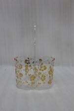 Clear acrylic spoon and cutlery holder featuring a gold floral design, divided compartments holding silverware and napkins, and a heart-shaped handle on a kitchen countertop