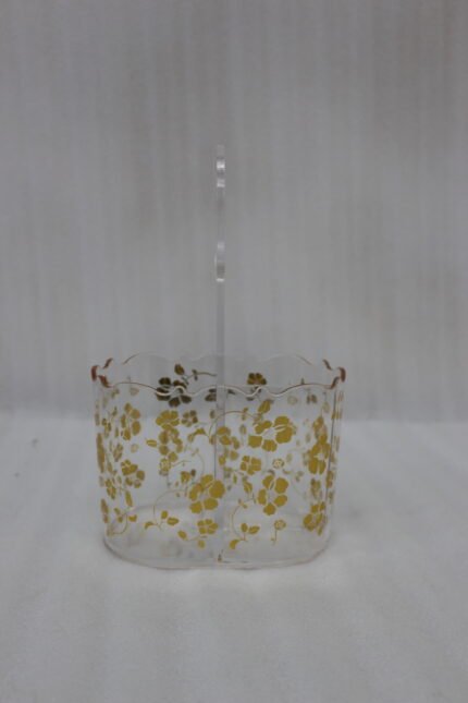 Clear acrylic spoon and cutlery holder featuring a gold floral design, divided compartments holding silverware and napkins, and a heart-shaped handle on a kitchen countertop