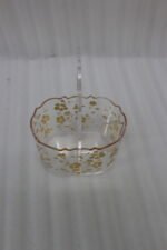 Clear acrylic spoon and cutlery holder featuring a gold floral design, divided compartments holding silverware and napkins, and a heart-shaped handle on a kitchen countertop