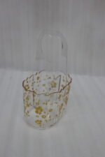 Clear acrylic spoon and cutlery holder featuring a gold floral design, divided compartments holding silverware and napkins, and a heart-shaped handle on a kitchen countertop