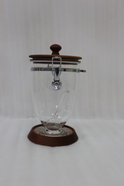 Set of three clear acrylic jars of varying sizes with wooden bases, wooden lids, airtight metal clamps, and hanging acrylic spoons on a kitchen countertop.