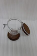 Set of three clear acrylic jars of varying sizes with wooden bases, wooden lids, airtight metal clamps, and hanging acrylic spoons on a kitchen countertop.