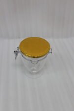 Three clear luxury acrylic storage jars of varying sizes featuring gold lids and secure silver airtight locking clasps, arranged on a marble countertop in a modern kitchen.