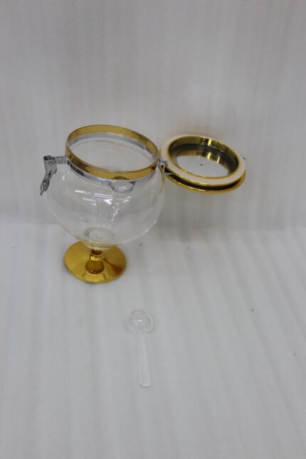 Three graduated luxury clear acrylic storage jars on pedestals with gold bases, matching gold lids, silver locking latches, and spoons arranged on a marble countertop.